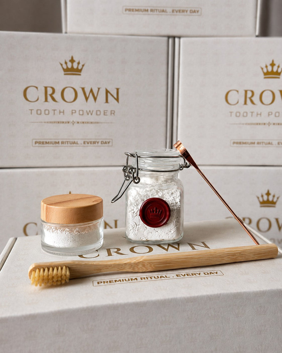 The square glass Crown jar of tooth powder with its red wax crown seal, shown with the glass travel jar, bamboo brush, and copper tongue scraper.