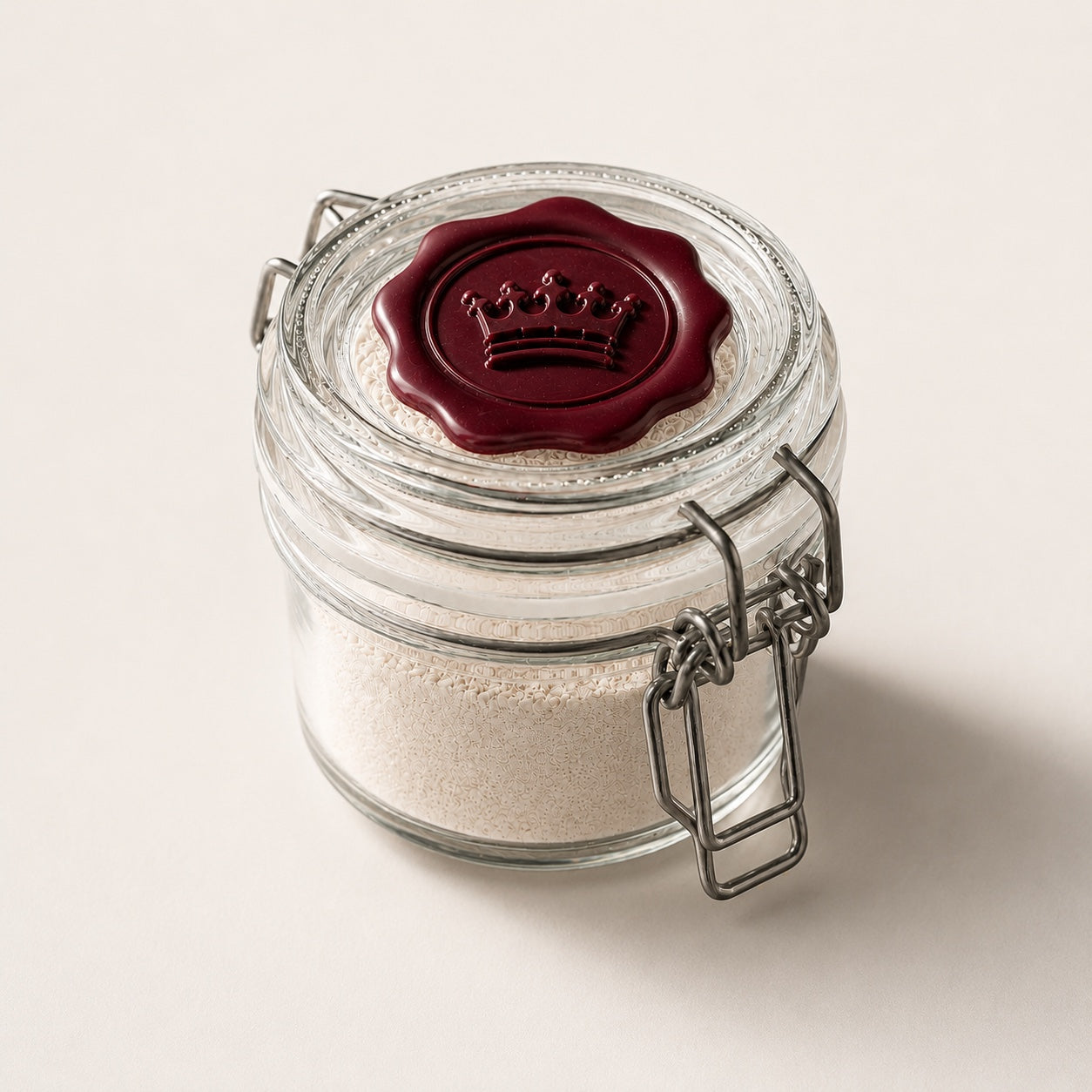 A sealed glass jar of white tooth powder topped with a burgundy wax crown seal on a pale background